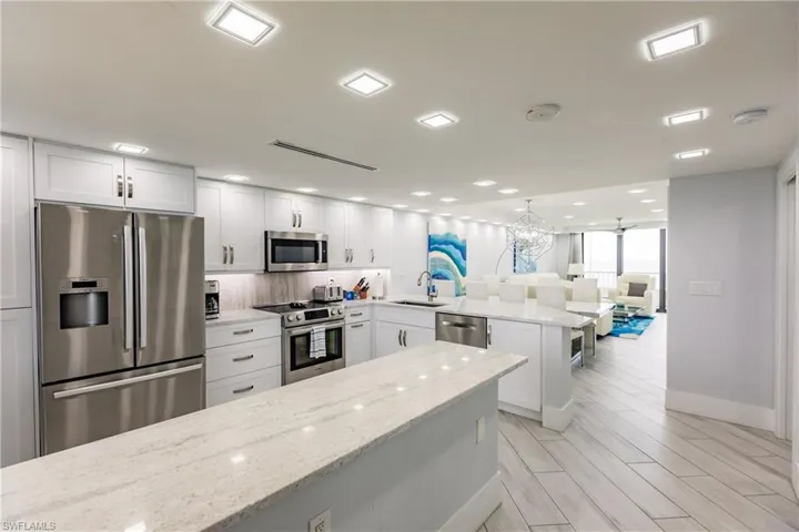 Kitchen with stainless steel appliances, a peninsula, wood tiled floors, light stone countertops, and white cabinetry