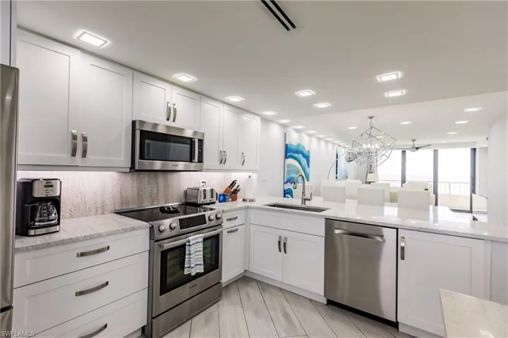 Kitchen featuring stainless steel appliances, suspended lighting, white cabinets, and light stone counters