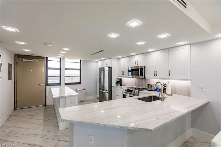 Kitchen with a peninsula, light stone countertops, stainless steel appliances, a center island, and white cabinets