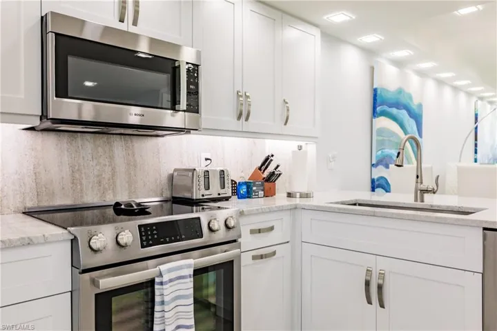 Kitchen with stainless steel appliances, white cabinetry, and light stone counters