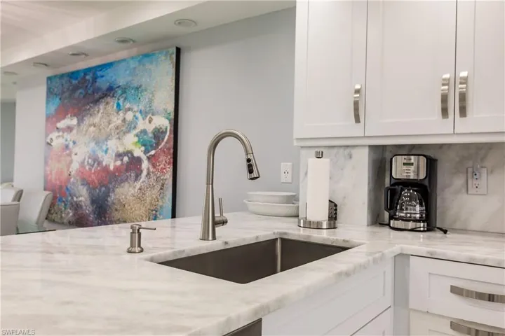 Kitchen featuring light stone counters, white cabinets, and backsplash