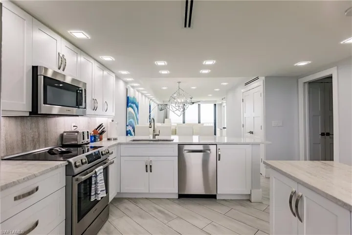 Kitchen featuring stainless steel appliances, white cabinetry, a chandelier, a peninsula, and light stone countertops