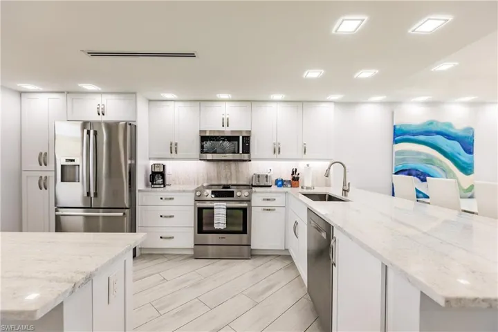 Kitchen featuring stainless steel appliances, white cabinetry, light stone counters, decorative backsplash, and a peninsula