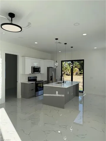 Kitchen featuring dual tone cabinets, range, a center island with sink, stainless steel refrigerator, and hanging light fixtures