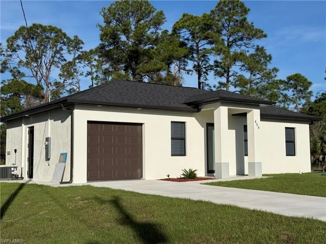 View of front facade with a front lawn, stucco siding, an attached garage, driveway, and roof with shingles