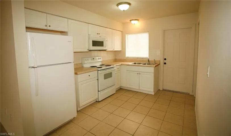 Kitchen featuring white appliances, white cabinets, light countertops, backsplash, and light tile patterned floors