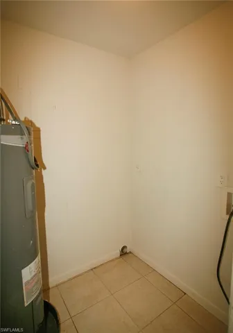 Washroom with electric water heater, light tile patterned floors, and washer hookup