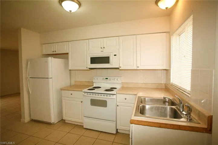 Kitchen featuring white appliances, white cabinets, light countertops, backsplash, and light tile patterned flooring