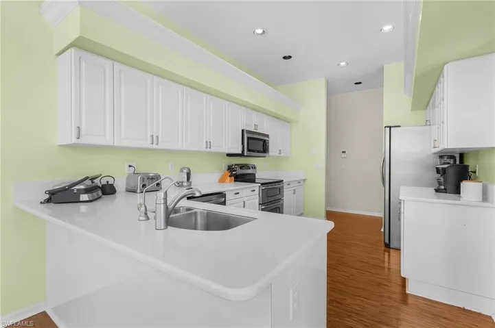 Kitchen with appliances with stainless steel finishes, white cabinets, wood finished floors, a peninsula, and light countertops