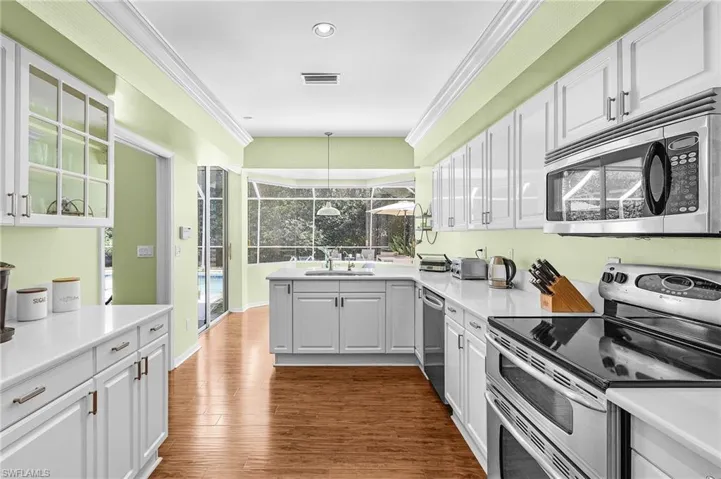 Kitchen featuring stainless steel appliances, white cabinetry, ornamental molding, light countertops, and dark wood-style floors