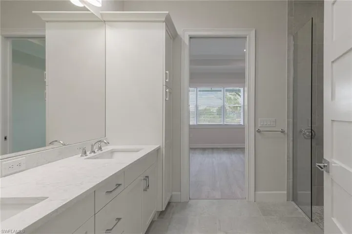 Bathroom featuring double vanity, a tile shower, baseboards, and a sink