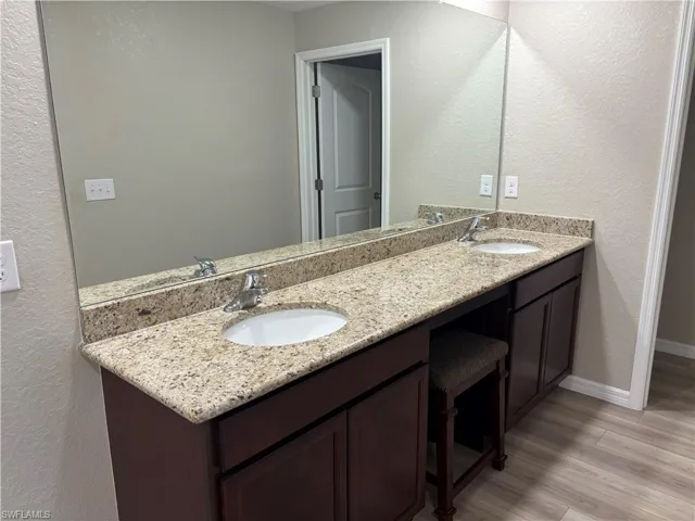 Full bathroom with a textured wall, double vanity, and light wood-style floors