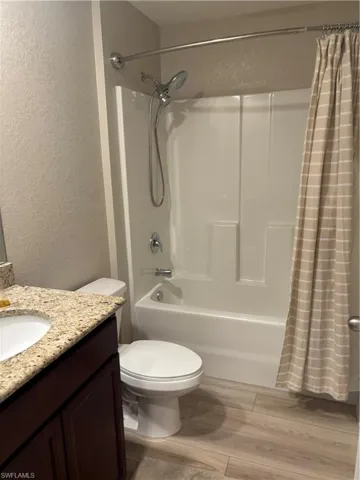 Full bathroom with a textured wall, shower / tub combo with curtain, light wood finished floors, and vanity