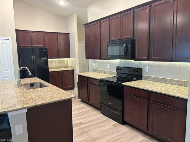Kitchen featuring black appliances, light stone counters, light wood-style flooring, a textured wall, and dark brown cabinets