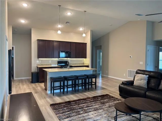 Kitchen featuring dark brown cabinets, a kitchen bar, light stone counters, open floor plan, and a kitchen island with sink