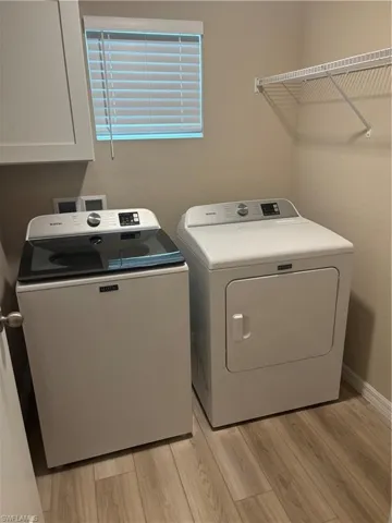 Laundry room with washing machine and dryer and light wood-style floors