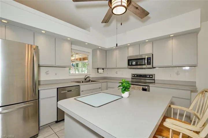 Kitchen with vaulted ceiling, a kitchen island, light tile patterned floors, stainless steel appliances, and sink