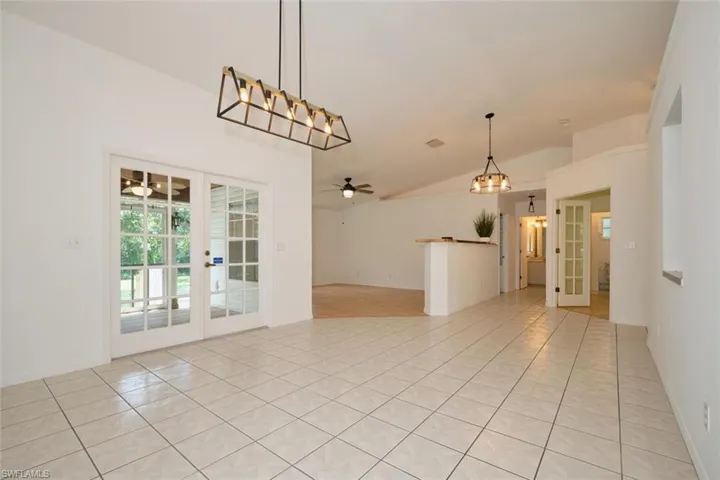 Spare room with ceiling fan with notable chandelier, vaulted ceiling, light tile patterned flooring, and french doors