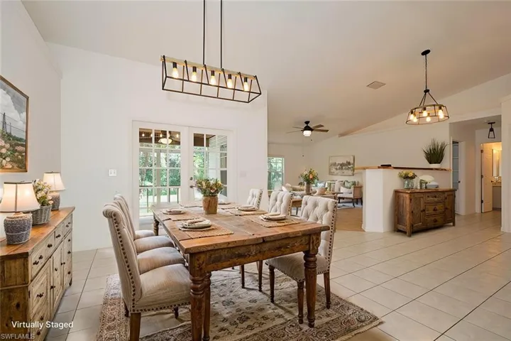 Tiled dining space featuring ceiling fan with notable chandelier and vaulted ceiling
