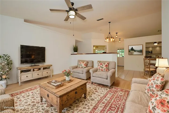 Living room with ceiling fan with notable chandelier, light hardwood / wood-style floors, and vaulted ceiling