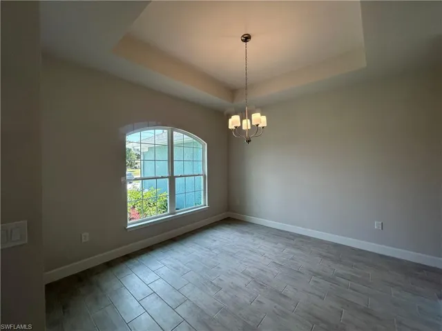 Formal Dining Room Featuring a Tray Ceiling, a Chandelier, and Wood Look Ceramic Tiled Flooring