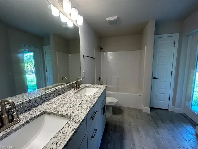 Full bath with Wood Look Ceramic Tiled Flooring, Dual vanities with Granite Countertops, Lots of Natural Light, and Tub/Shower Combination