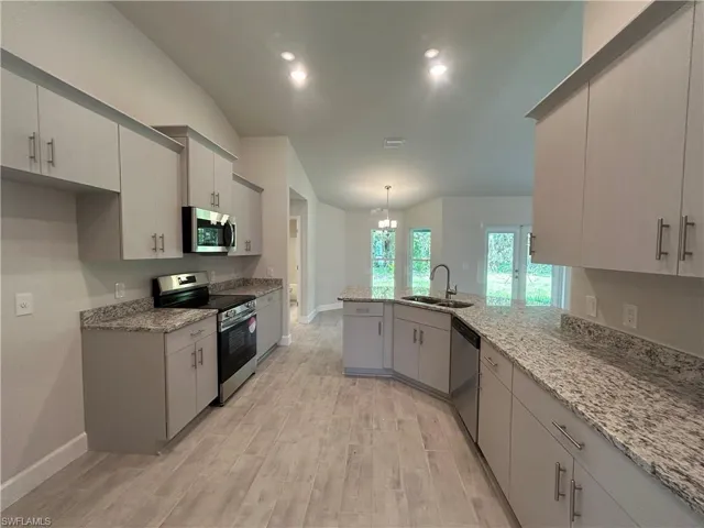 Kitchen Featuring Stainless Steel Appliances, Vaulted Ceiling, Granite Countertops, Wood Look Ceramic Tiled Floor, and Recessed LED Lighting