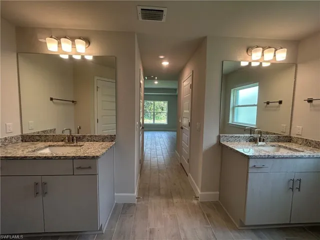 Primary Bathroom Featuring Dual Vanities with Granite Countertops, Wood Look Ceramic Tiled Flooring, and Recessed LED Lighting