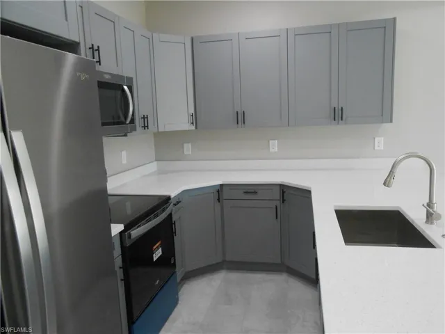 Kitchen with gray cabinetry, stainless steel appliances, and light stone countertops