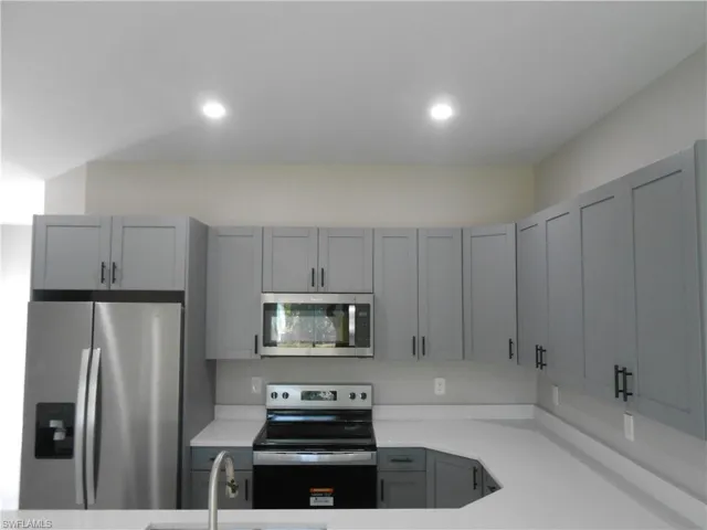Kitchen with appliances with stainless steel finishes, gray cabinetry, light stone countertops, and recessed lighting