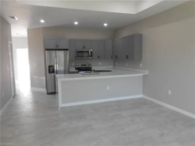 Kitchen with appliances with stainless steel finishes, gray cabinets, a peninsula, recessed lighting, and a kitchen breakfast bar