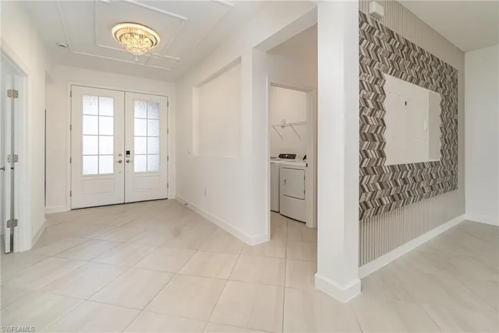 Foyer entrance featuring hanging lights, washing machine and clothes dryer, light tile patterned flooring, and french doors