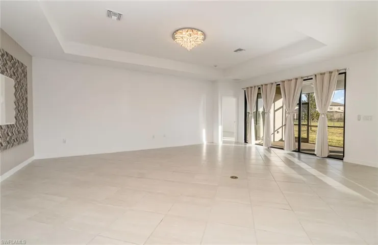 Empty room featuring a tray ceiling, light tile patterned flooring, and suspended lighting