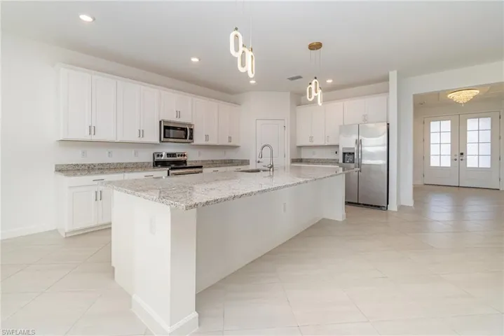Kitchen with stainless steel appliances, light stone countertops, white cabinets, a center island with sink, and light tile patterned floors