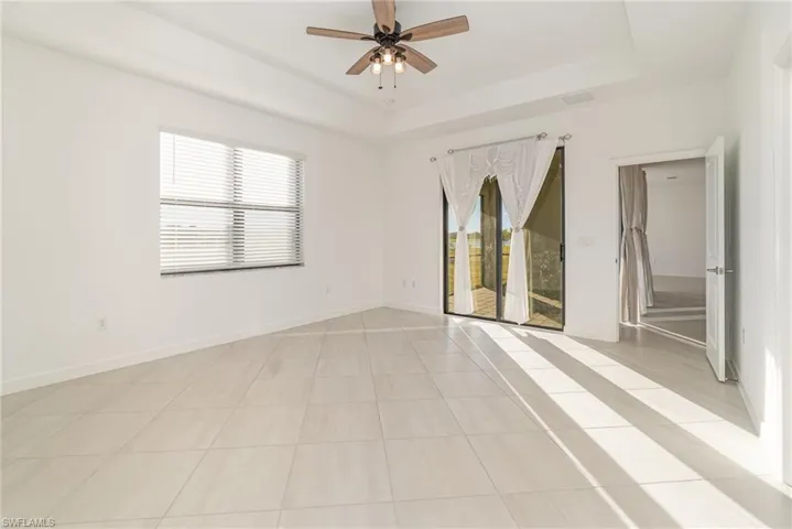 Unfurnished room featuring light tile patterned floors, a ceiling fan, and a tray ceiling