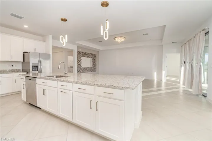 Kitchen with a raised ceiling, white cabinetry, stainless steel appliances, light stone countertops, and pendant lighting