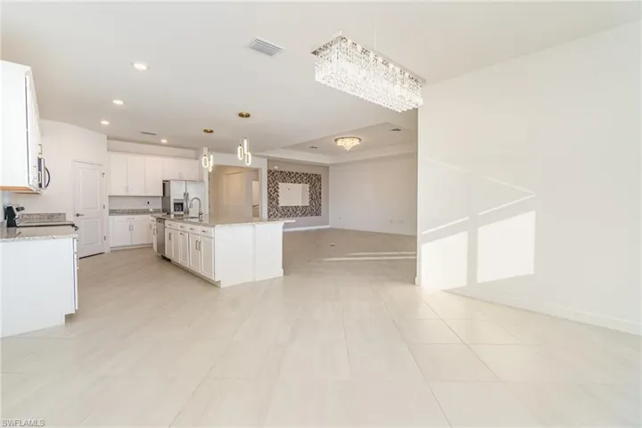 Kitchen featuring light stone counters, open floor plan, white cabinetry, a center island with sink, and stainless steel refrigerator with ice dispenser