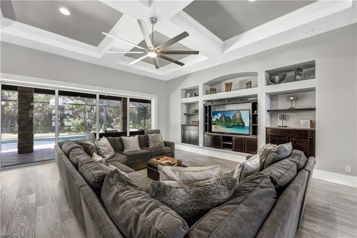 Living room featuring coffered ceiling, ceiling fan, crown molding, and wood-type flooring