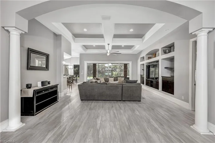 Living room with coffered ceiling, light hardwood / wood-style floors, ceiling fan, beamed ceiling, and decorative columns