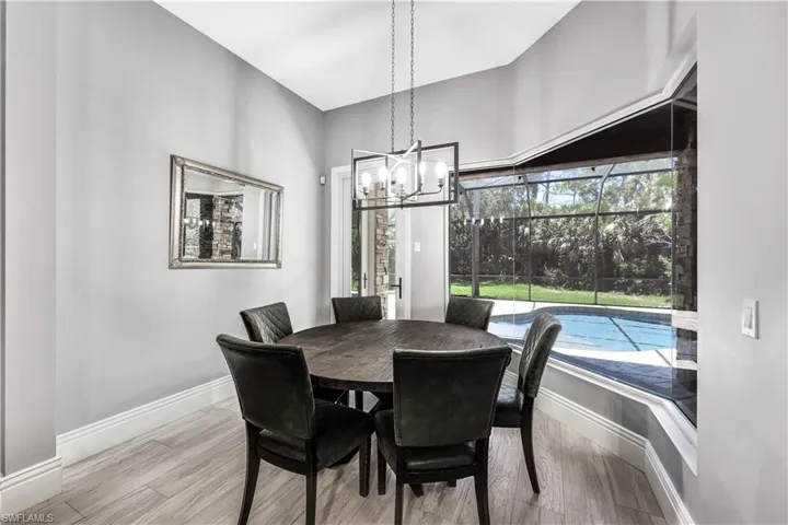Dining area off kitchen featuring a chandelier and light hardwood / wood-style flooring and has view of pool area and woods.