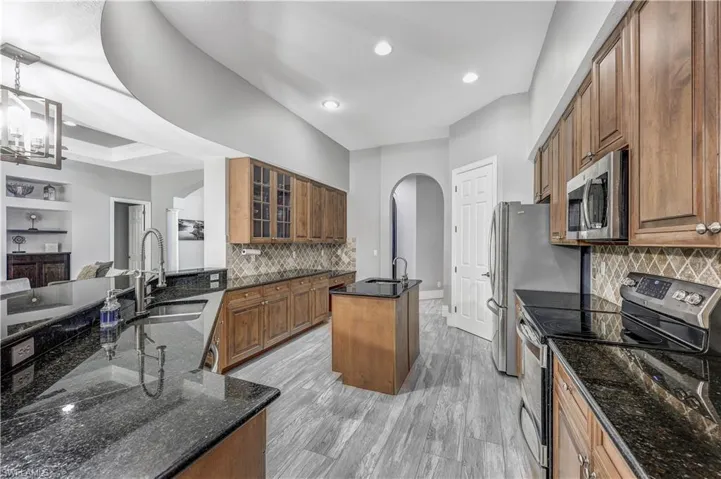 Kitchen featuring dark stone counters, light hardwood / wood-style flooring, stainless steel appliances, backsplash, and sink