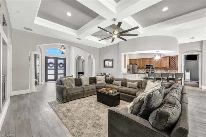 Living room with beam ceiling, coffered ceiling, light hardwood / wood-style flooring, and ceiling fan with notable chandelier