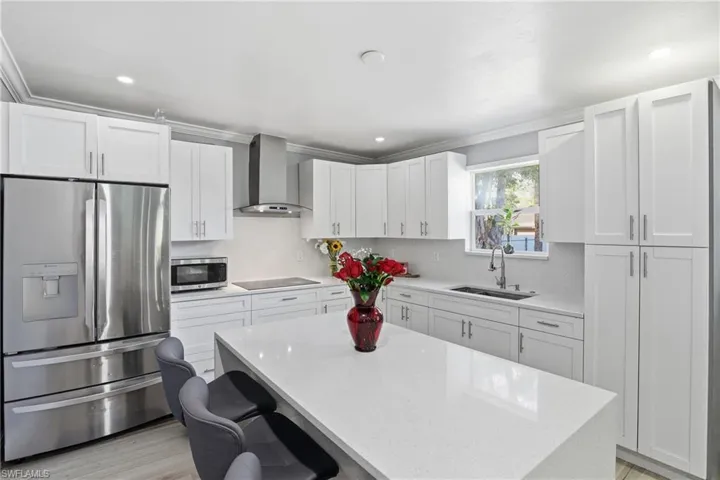 Kitchen featuring stainless steel appliances, light stone counters, white cabinets, light wood-style flooring, and a center island