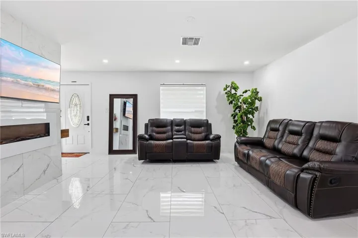 Living room with a large fireplace, recessed lighting, and light marble finish floors