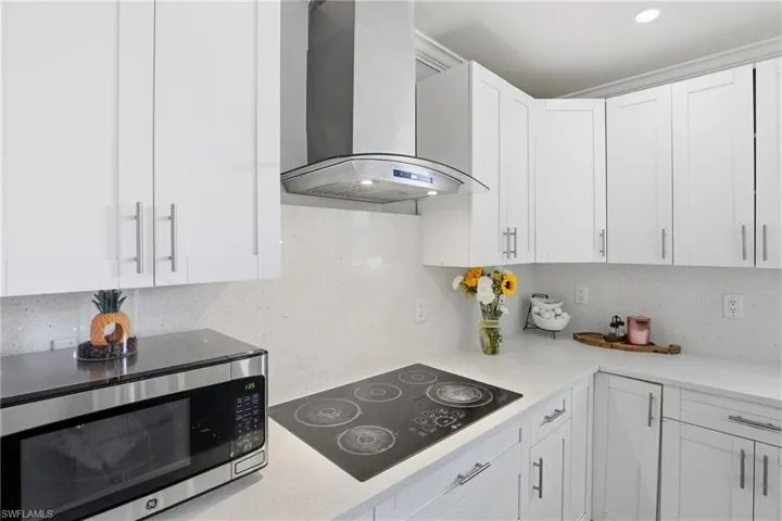 Kitchen with stainless steel microwave, black electric stovetop, white cabinets, and light stone countertops