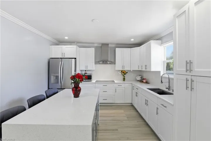 Kitchen with light stone counters, stainless steel fridge with ice dispenser, ornamental molding, white cabinets, and recessed lighting