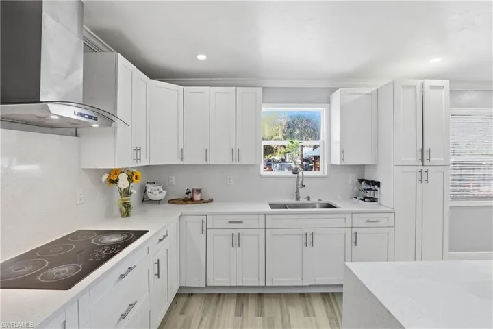 Kitchen featuring black electric cooktop, light stone countertops, light wood-type flooring, white cabinets, and decorative backsplash