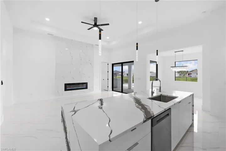 Kitchen with dishwasher, sink, a raised ceiling, a fireplace, and hanging light fixtures