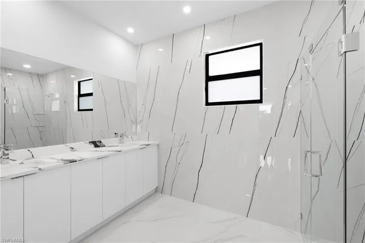 Bathroom featuring a wealth of natural light, a shower with door, vanity, and tile walls