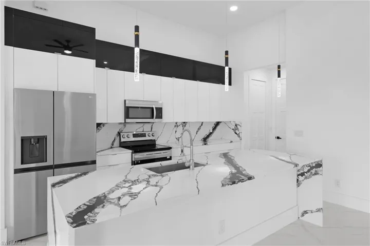 Kitchen featuring stainless steel appliances, decorative backsplash, light stone countertops, white cabinets, and ceiling fan